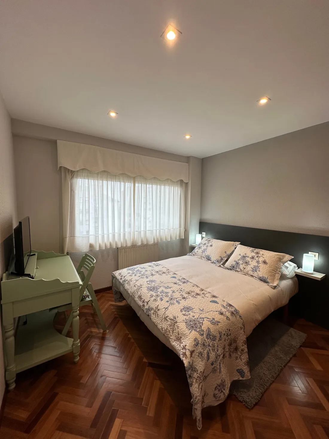 Dormitorio del Apartamento Villaluz con cama de matrimonio, ropa de flores azules y escritorio verde